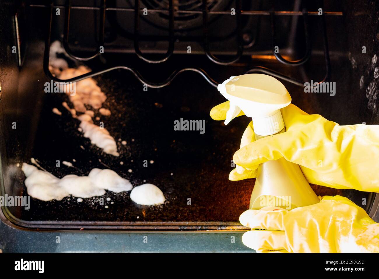 cleaning oven in home kitchen - hands in gloves spray a reagent on dirty bottom of oven Stock Photo
