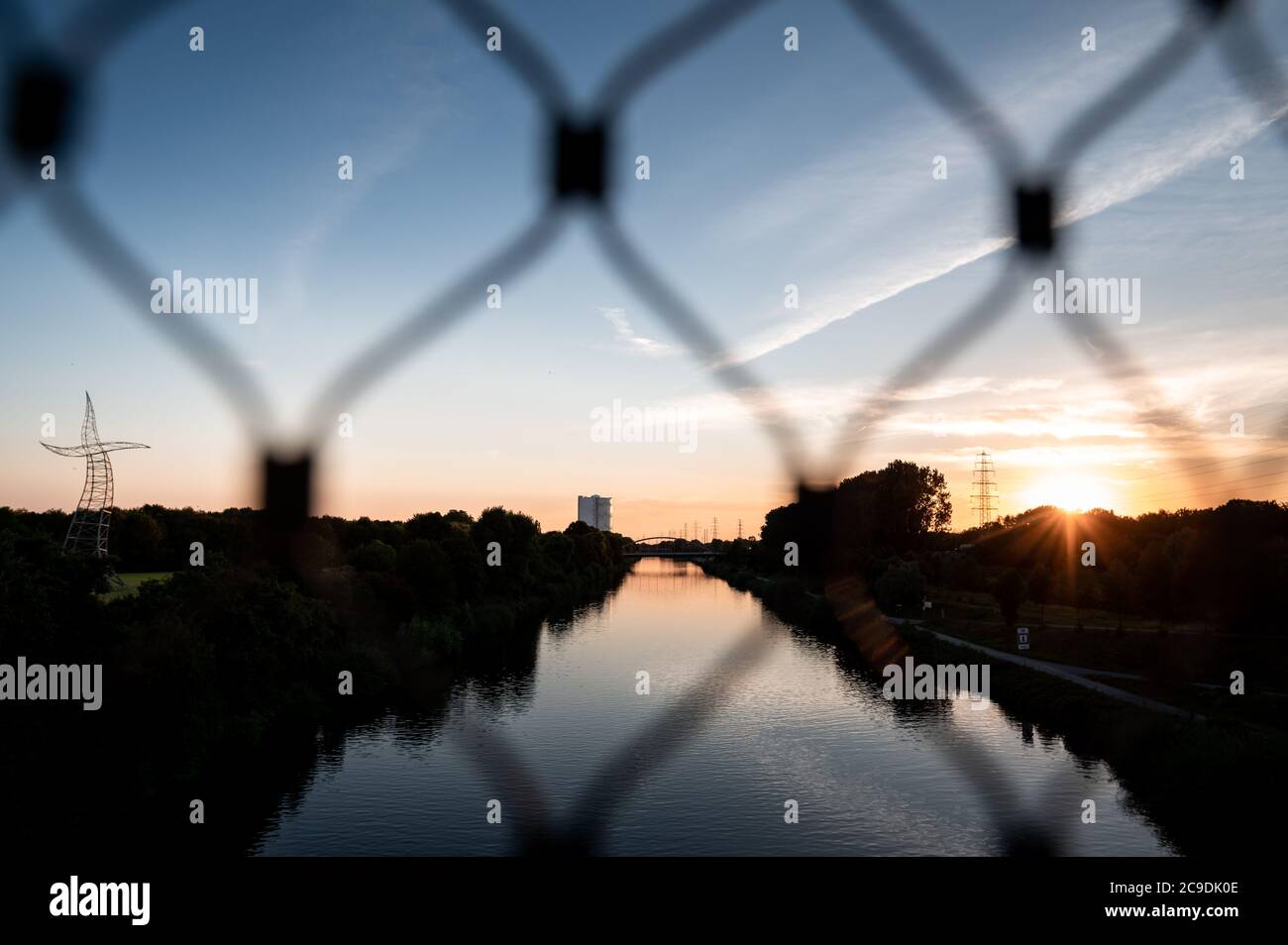 Oberhausen, Germany. 30th July, 2020. The sun sets behind the Rhine-Herne-Canal while the art installation 'Sorcerer's Apprentice' and the Gasometer Oberhausen can be seen in the background. With temperatures of up to 36 degrees, lots of sunshine and few clouds, Friday will probably be the hottest day of the year in NRW. For the region from Cologne to Aachen, the German Weather Service (DWD) expects maximum values between 34 and 36 degrees Celsius. Credit: Fabian Strauch/dpa/Alamy Live News Stock Photo