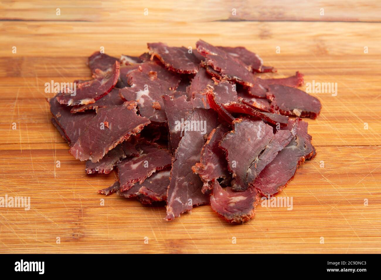 Pile of thinly sliced Turkish traditional pastirma (pastrami) on wooden chopping board with copy space for text, close up Stock Photo