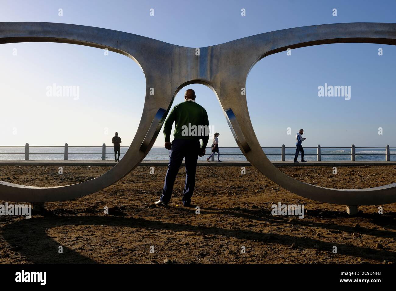 Everyday life on the promenade with Michael Elion's Madiba (Nelson Mandela) inspired public sculpture 'Perceiving Freedom' in Sea Point, Cape Town. Stock Photo