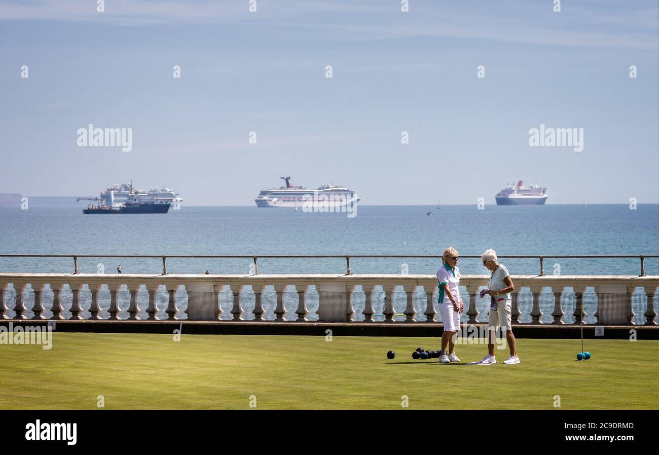 Pair of mature ladies playing bowls in front of collection of large cruise ships moored in Weymouth Bay  because of Coronavirus - in Weymouth, Dorset, Stock Photo