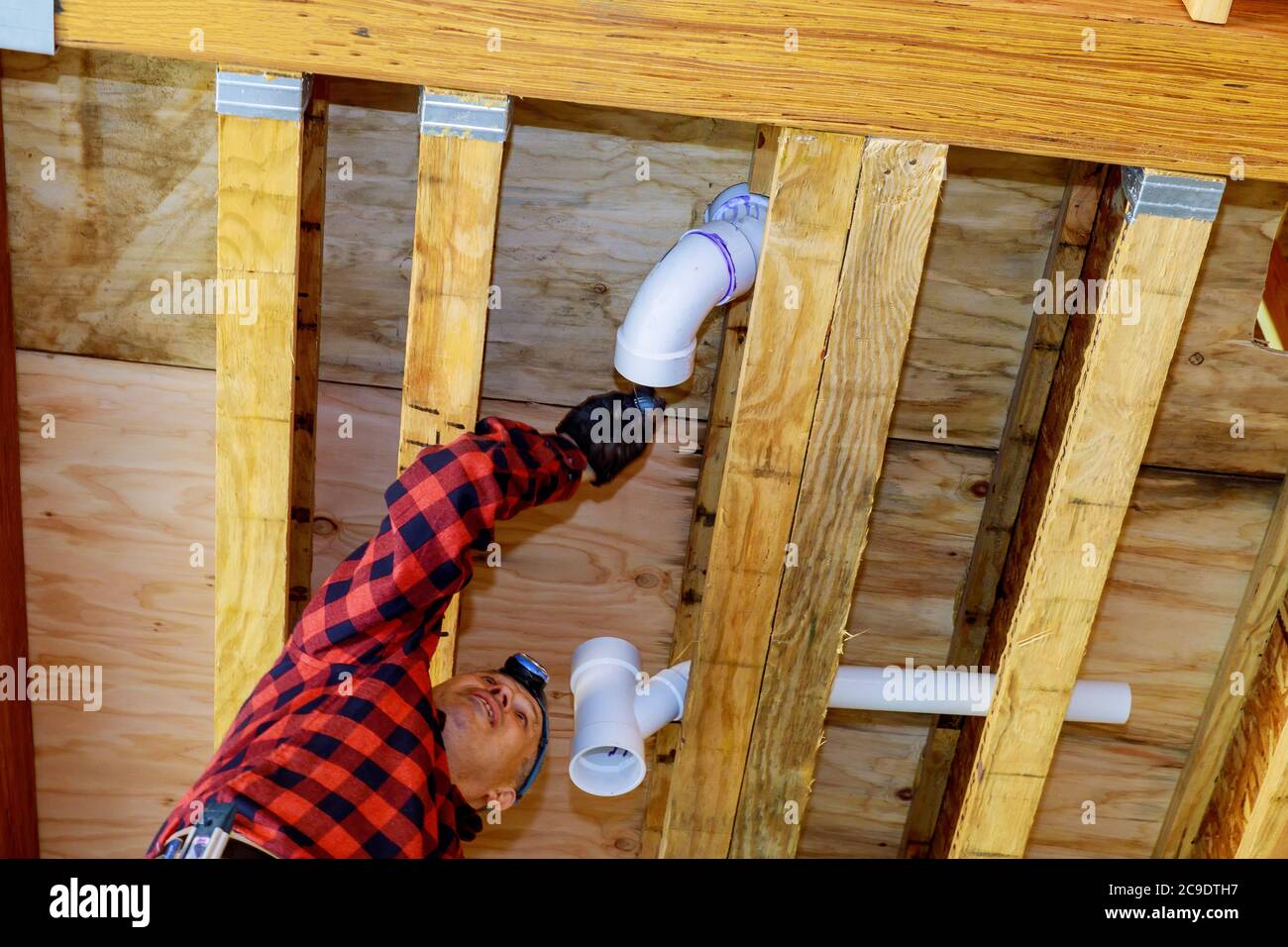 PVC plastic sewer toilet white pipe in the plumber gluing, on wooden frame ceiling beam of house Stock Photo