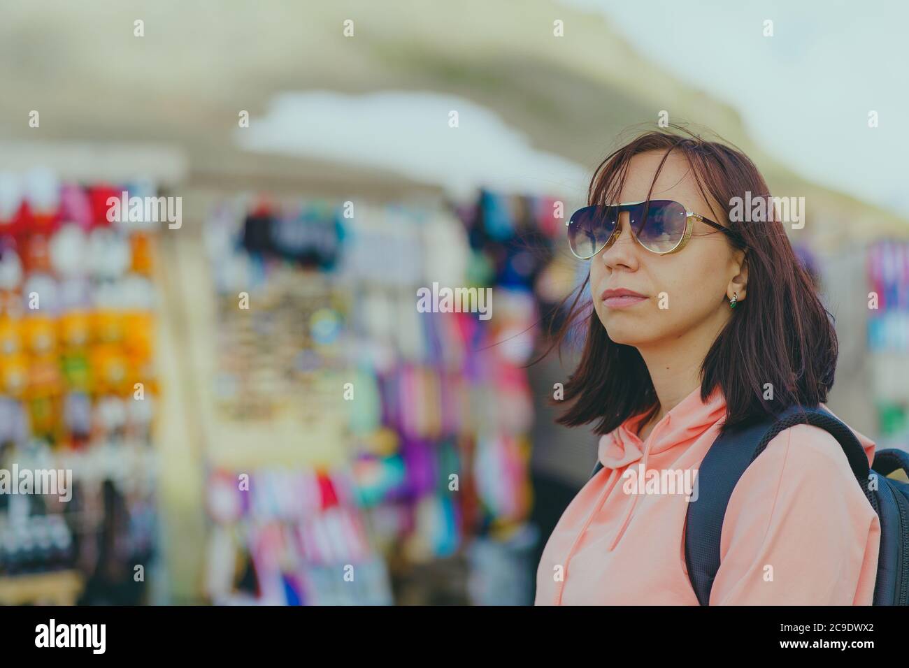 Female traveler on market in mountainous terrain. Woman tourist considering souvenirs in shopping booths. Stock Photo