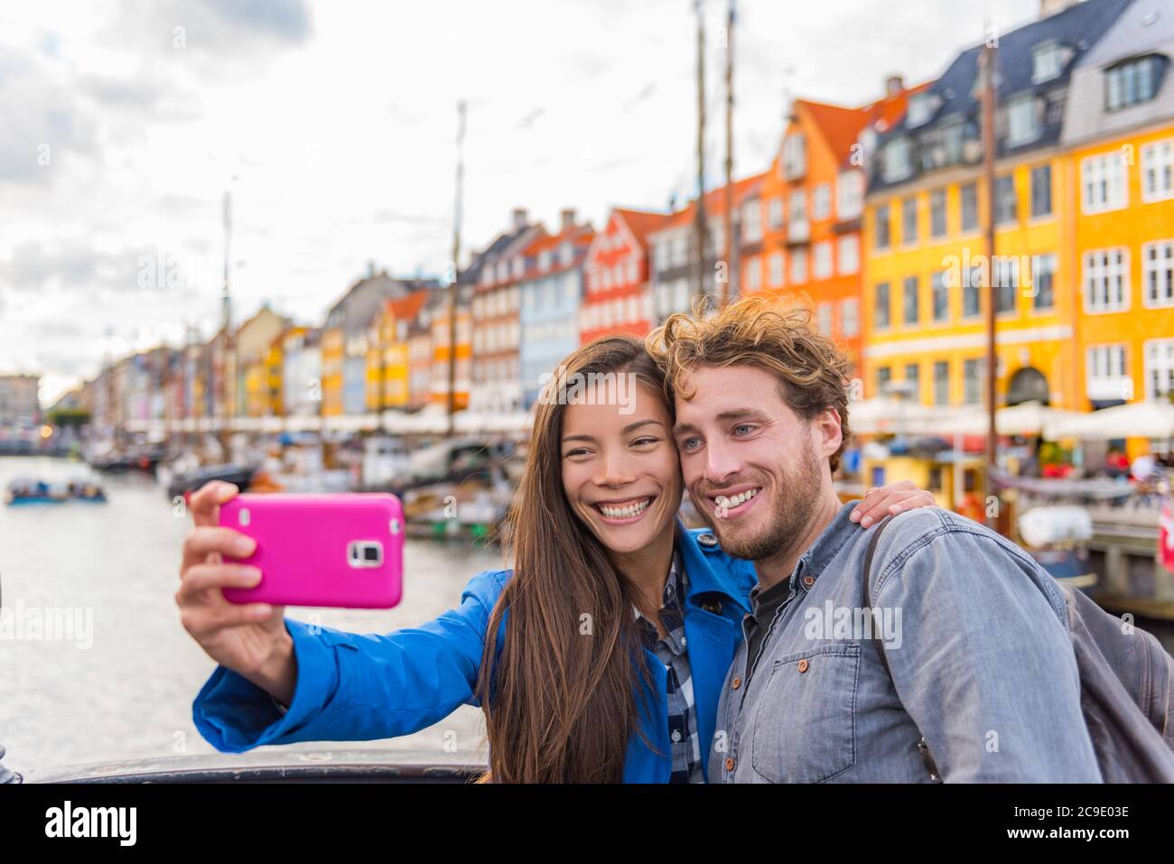 Copenhagen travel couple tourists taking selfie photo with phone camera. Smiling young people students at old port Nyhavn, tourism danish landmark in Stock Photo