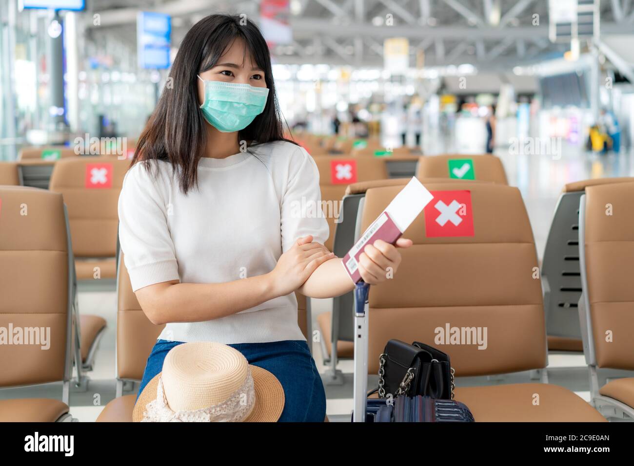 Asian woman tourist wearing mask looking happy while smiling behind the mask and sitting social distancing chair in airport terminal during protection Stock Photo