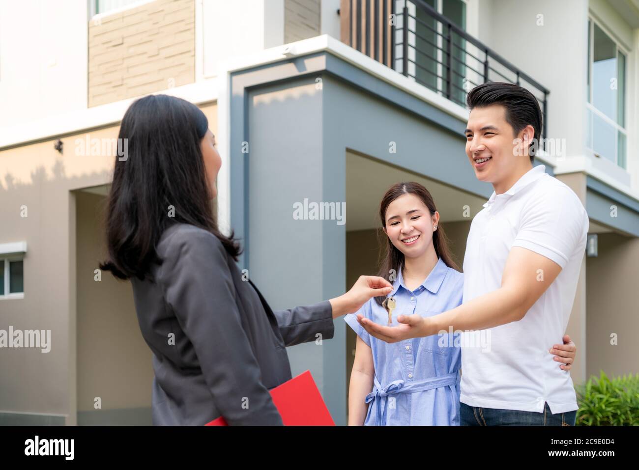 Asian happy smile young couple take keys new big house from real estate agent or realtor in front of their house after signing contract agreement, con Stock Photo