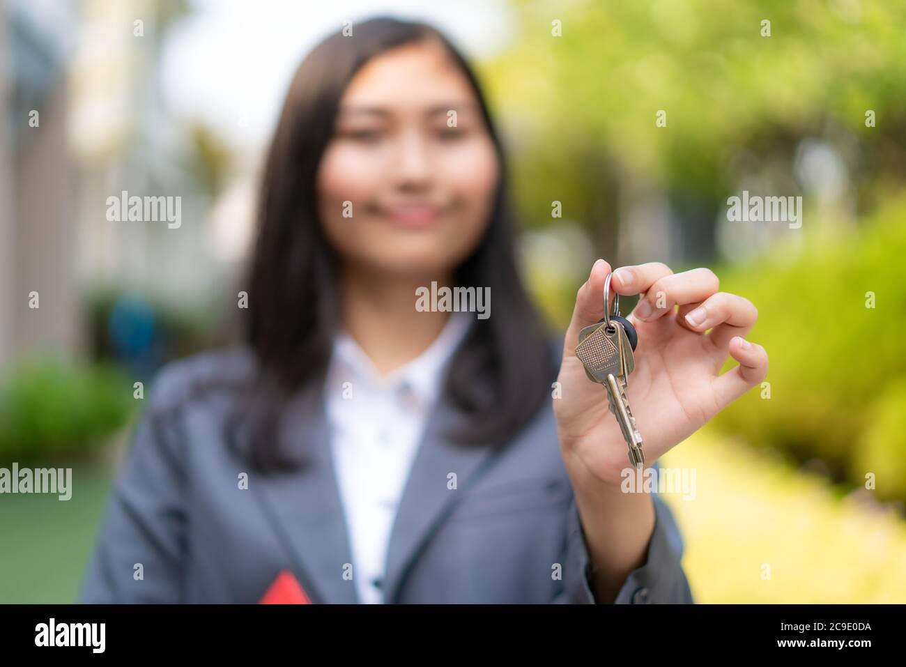 Asian real estate agent or realtor woman smiling and holding red file with showing house key in front of thier house in summer day. Stock Photo