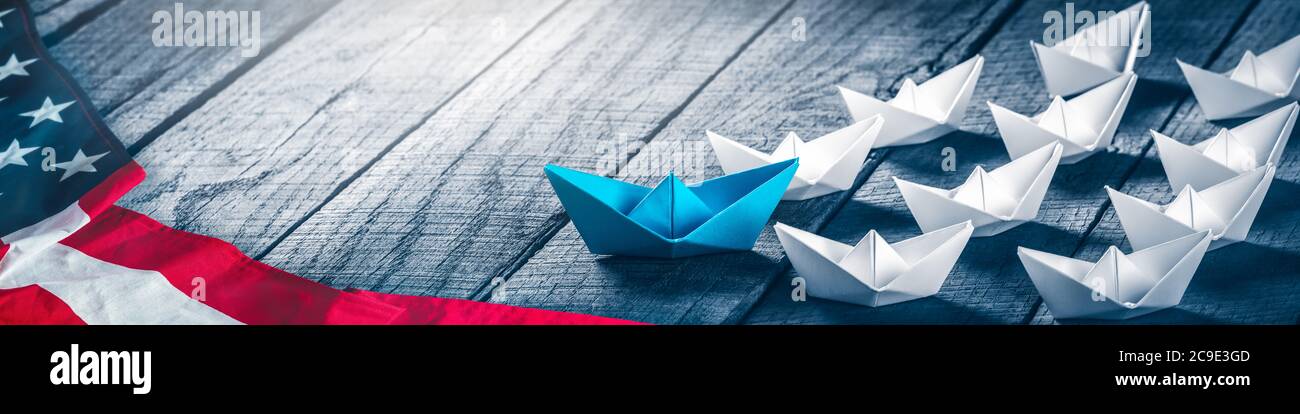 Blue Paper Boat Leading A Fleet Of Small White Boats With American Flag On Wooden Table - Democratic Leadership / Election Concept Stock Photo