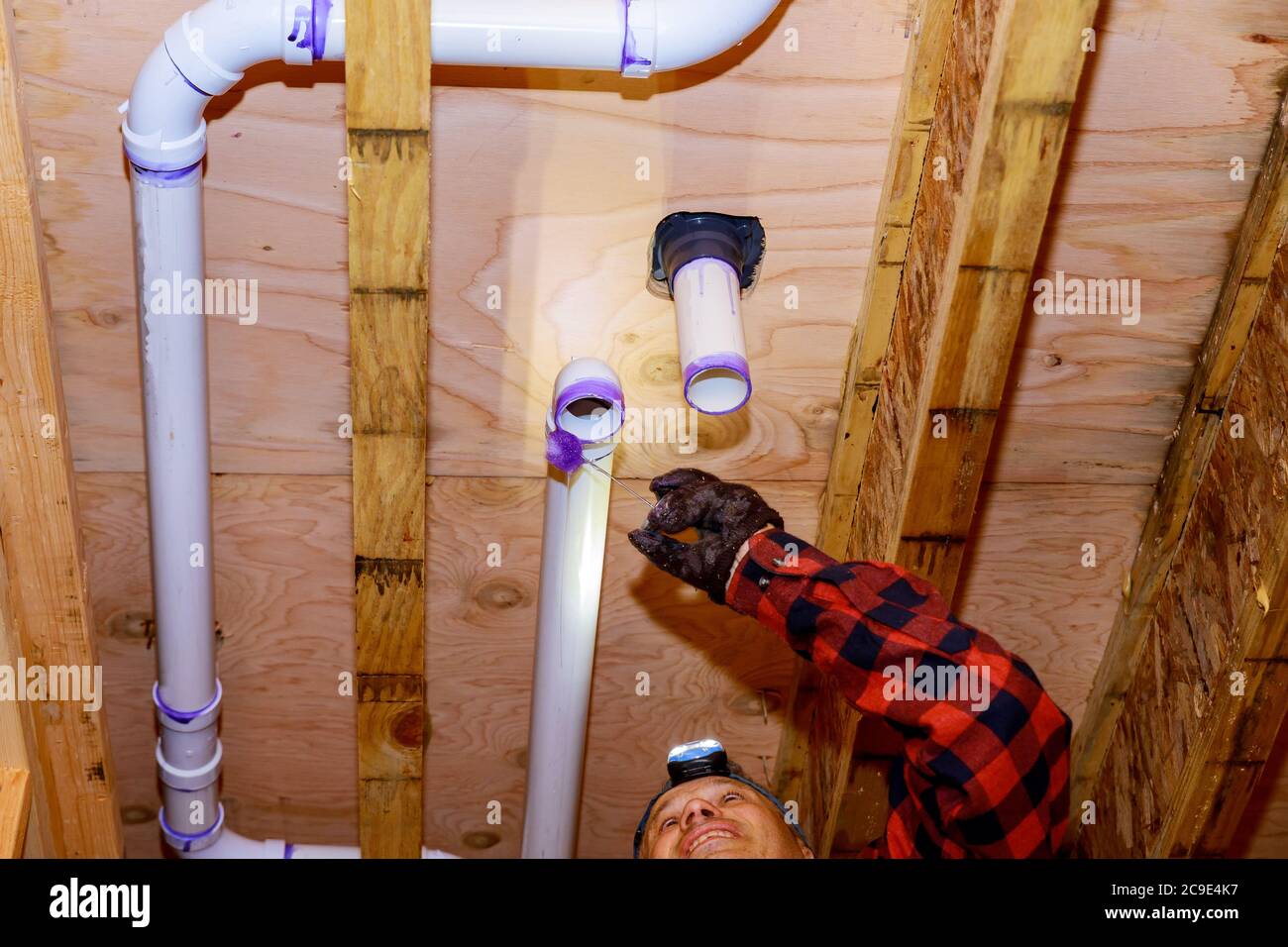 Plumber gluing PVC plastic sewer toilet white pipe on wooden frame ceiling beam of house soft focus Stock Photo