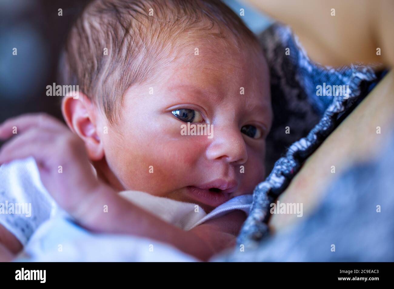 A newborn wearing a white cap baby rest on his mothers chest and stares into the camera Stock