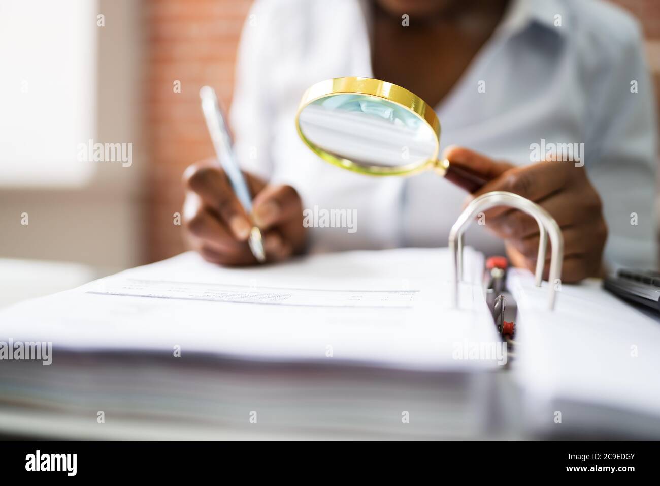 Auditor Investigating Business Fraud Using Magnifying Glass In Office Stock Photo