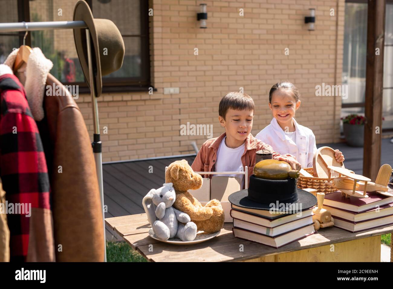 Positive curious children standing at table with toys and books and viewing garage stuff while choosing it to buy Stock Photo
