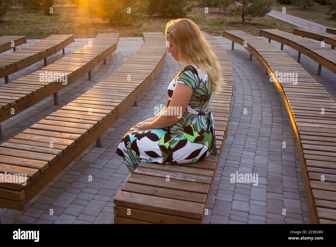 The girl is sitting alone in her back among the many benches of the street theater Stock Photo