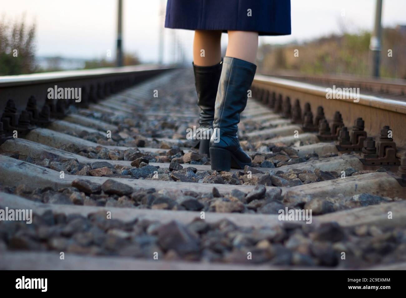 Girl walks on railway rails in a coat and boots - travel, depression, lifestyle Stock Photo