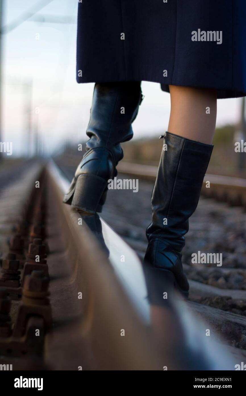 Girl walks on railway rails in a coat and boots - travel, depression, lifestyle Stock Photo