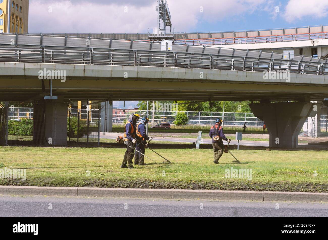 Saint Petersburg, Russia - July 26, 2020: Three workers in overalls mow the grass on the lawn with trimmers Stock Photo