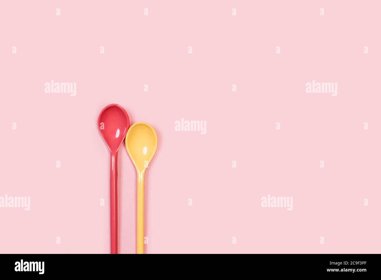 Two plastic colored spoons on a pink background Stock Photo
