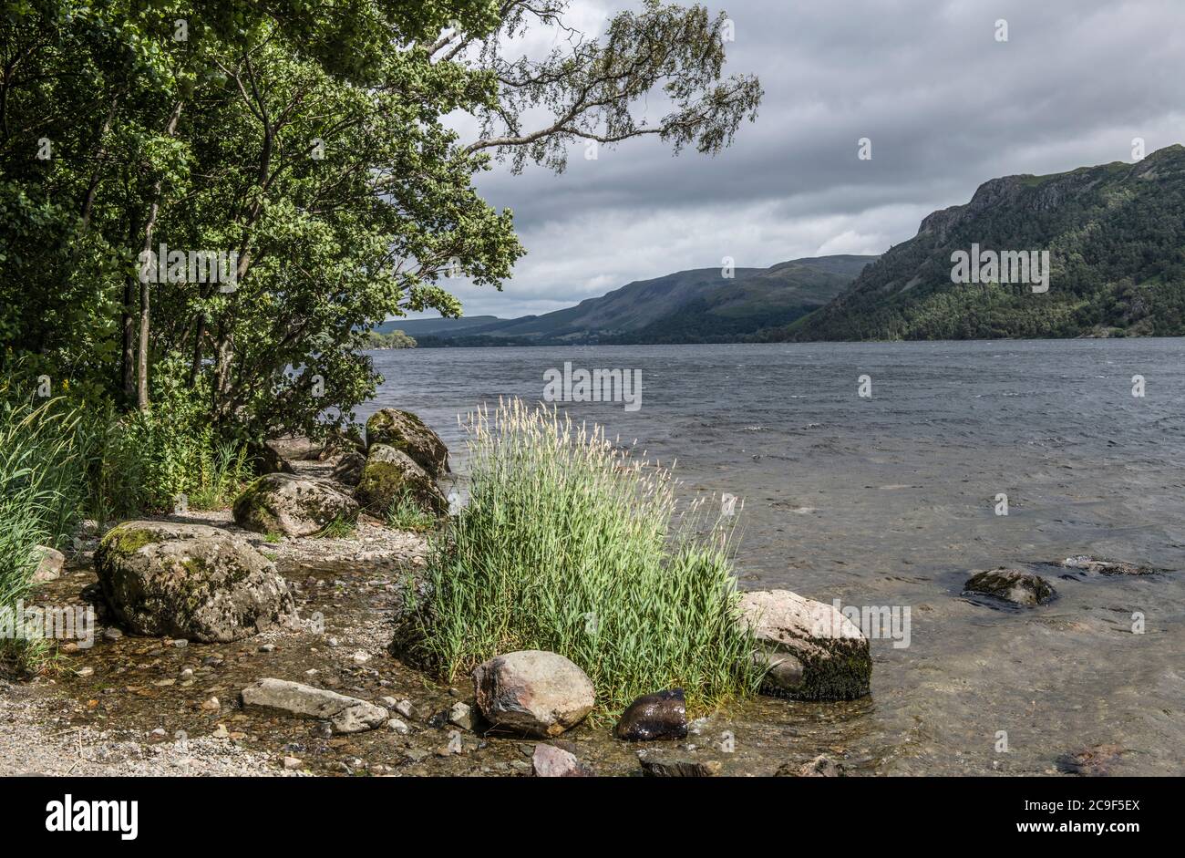 The shoreline of Ullswater in the Lake District National Park on a mixed weather summer afternoon. Stock Photo