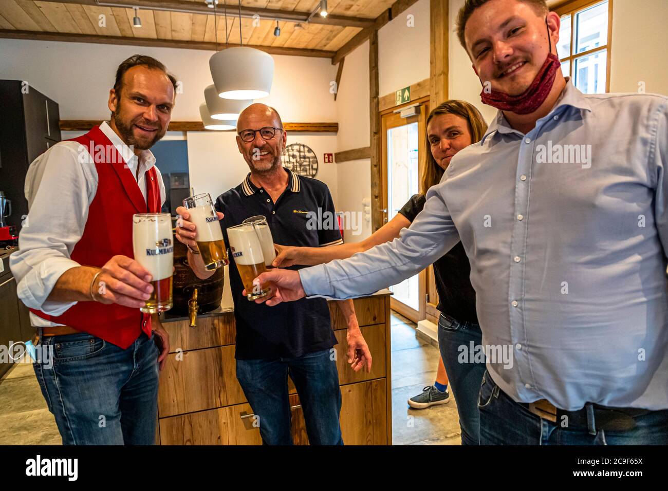 Beer sommelier Georg Hiernickel (l.) and three participants raise freshly tapped glasses of beer in a toast; one wears his face mask pulled down under his chin, a nod to 2020's coronavirus precautions, during the beer seminar at the Hollerhöfe in Kemnath-Waldeck, Upper Palatinate, Bavaria, Germany. Stock Photo