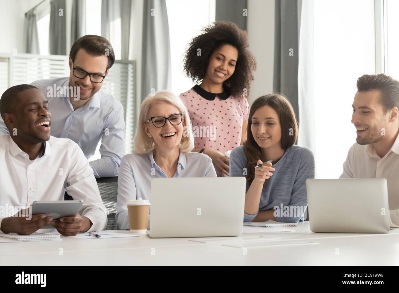Smiling mature mentor teaching diverse employees team, using laptop Stock Photo