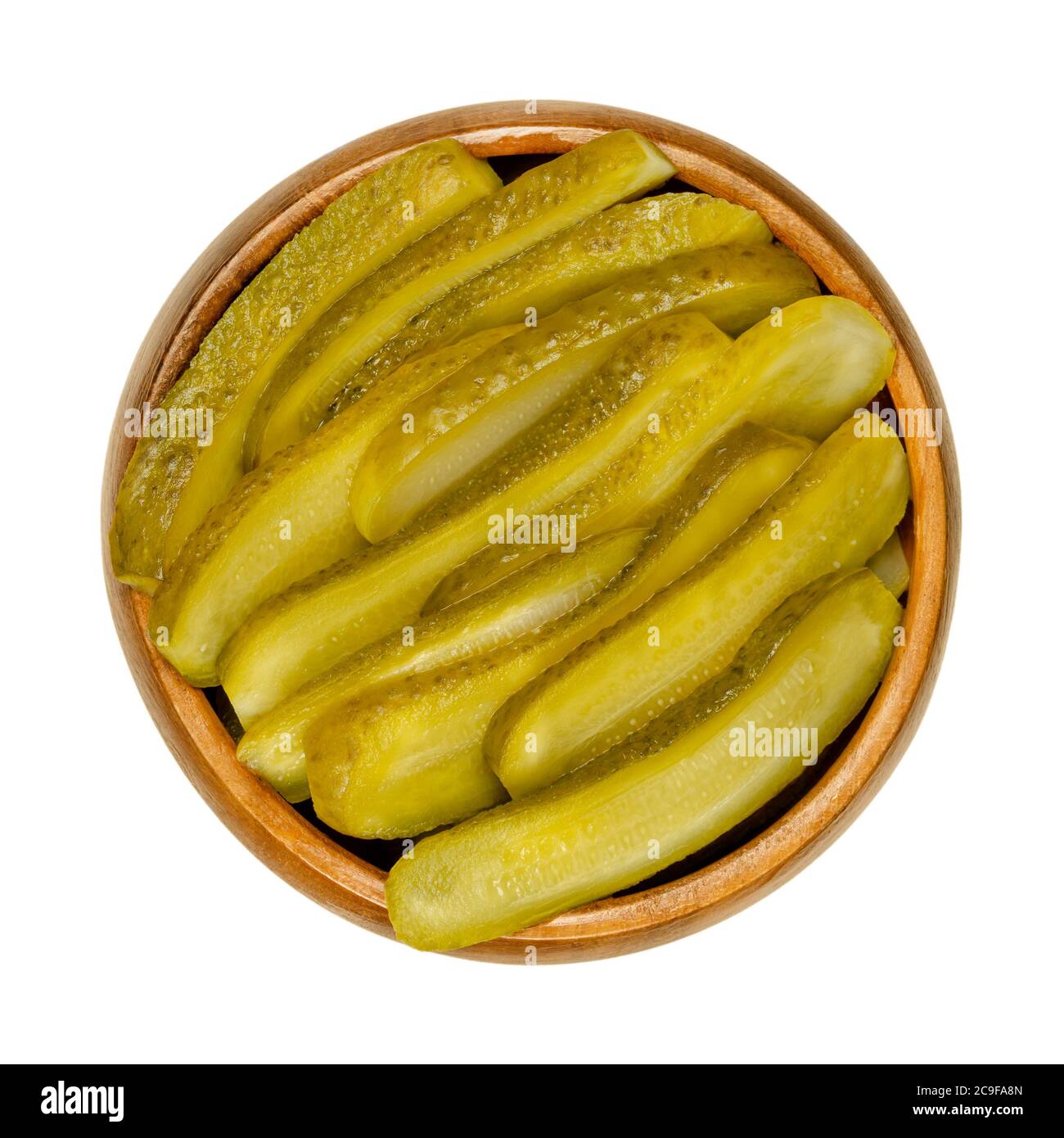Sliced pickled cucumbers, also known as pickle or gherkin, in a wooden bowl. Small pickled cucumbers with bumpy skin, sliced lengthways. Baby pickles. Stock Photo