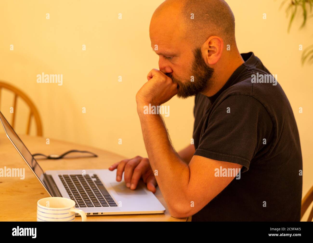 Young white Caucasian man looking worried sitting at table with laptop computer, UK Stock Photo