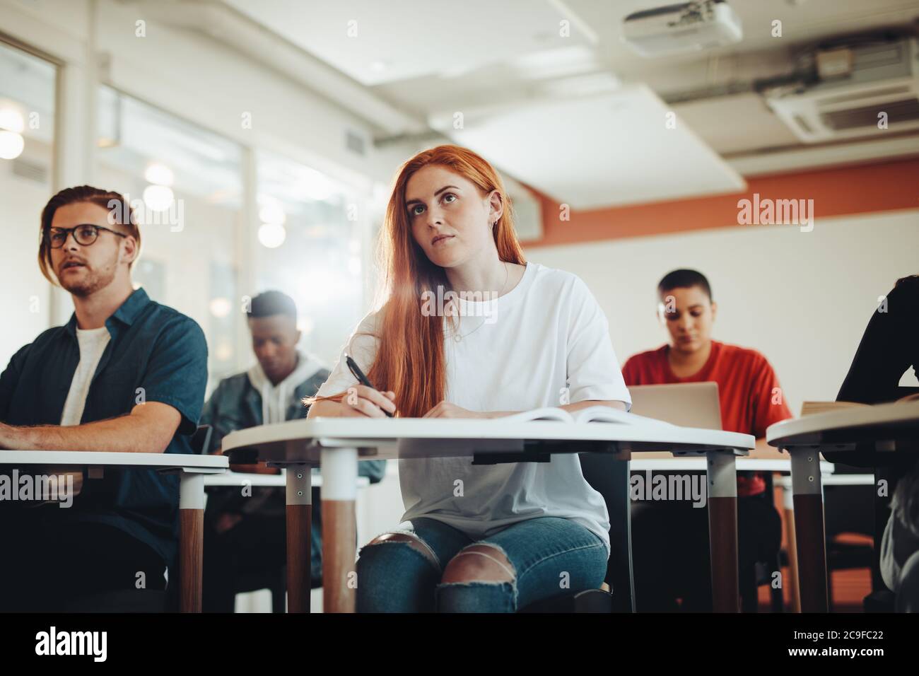 Pretty teenage student paying attention to lecture in classroom. Woman studying at the college classroom. Stock Photo