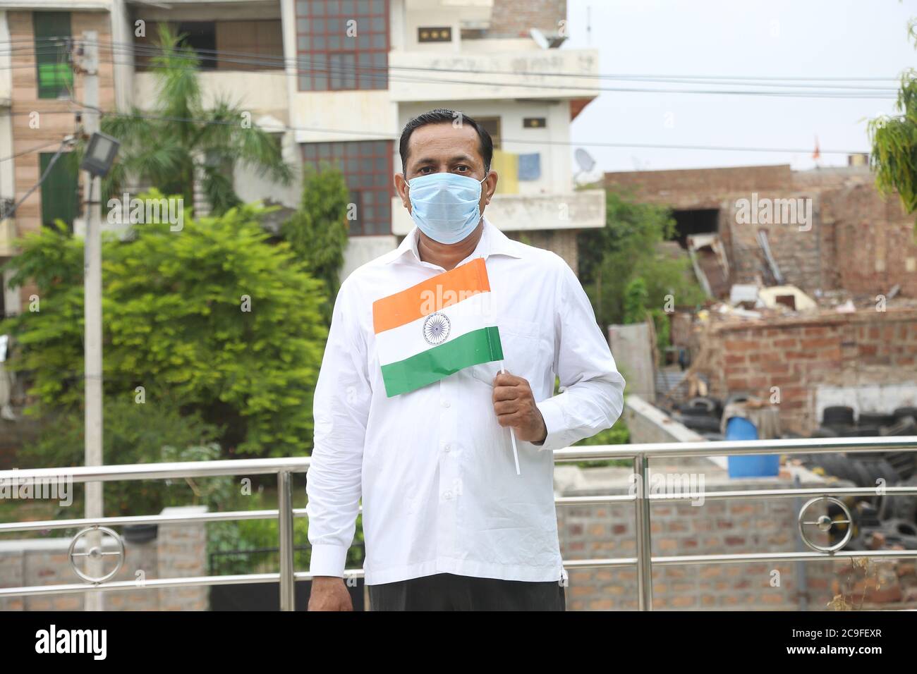 Mature man wearing mask holding waving indian tricolour flag outdoor, republic day or independence day concept during covid-19 pandemic. Stock Photo