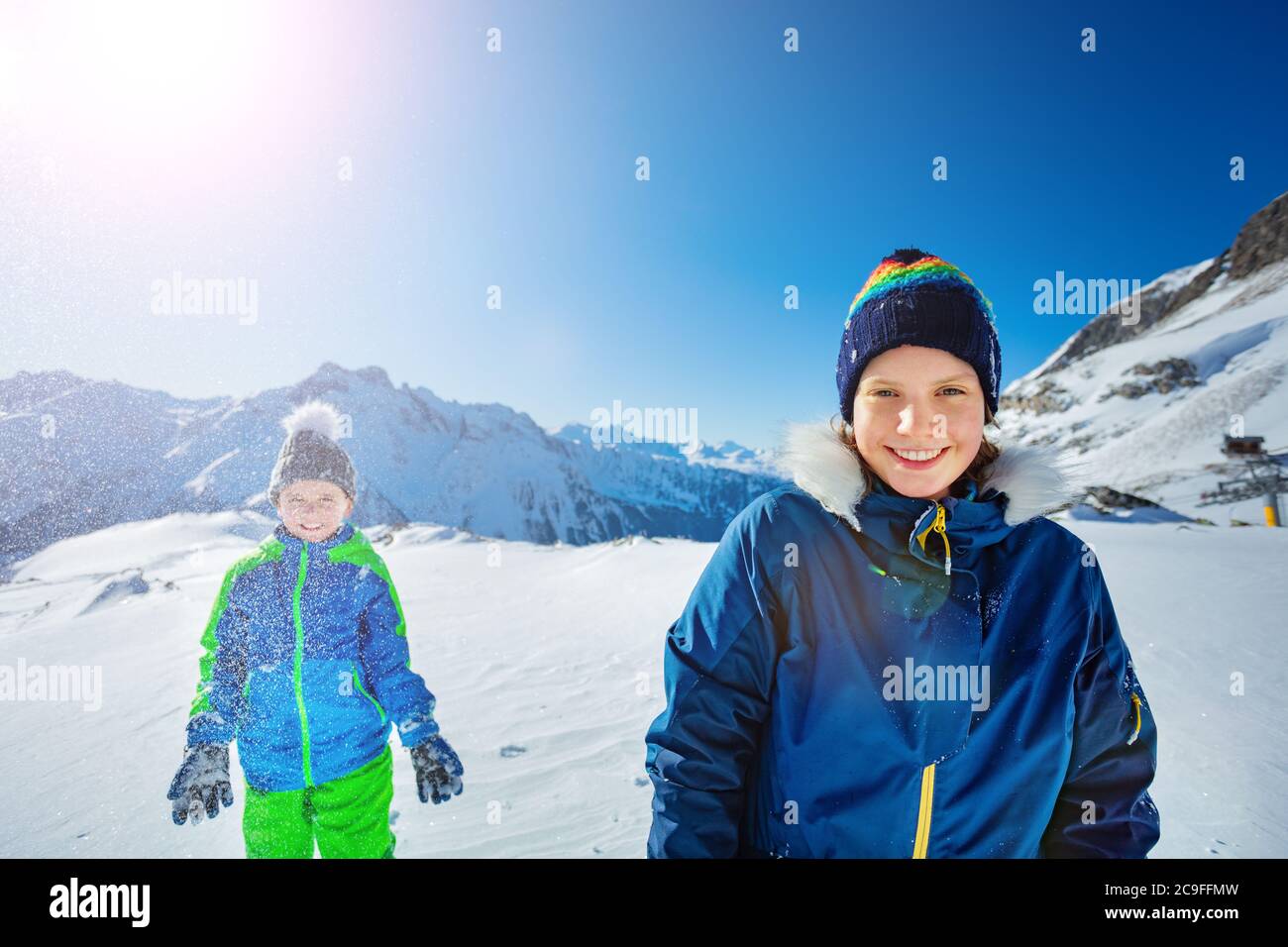 Two happy kids girl with boy have fun stand together throw snow in the air over beautiful mountain view Stock Photo