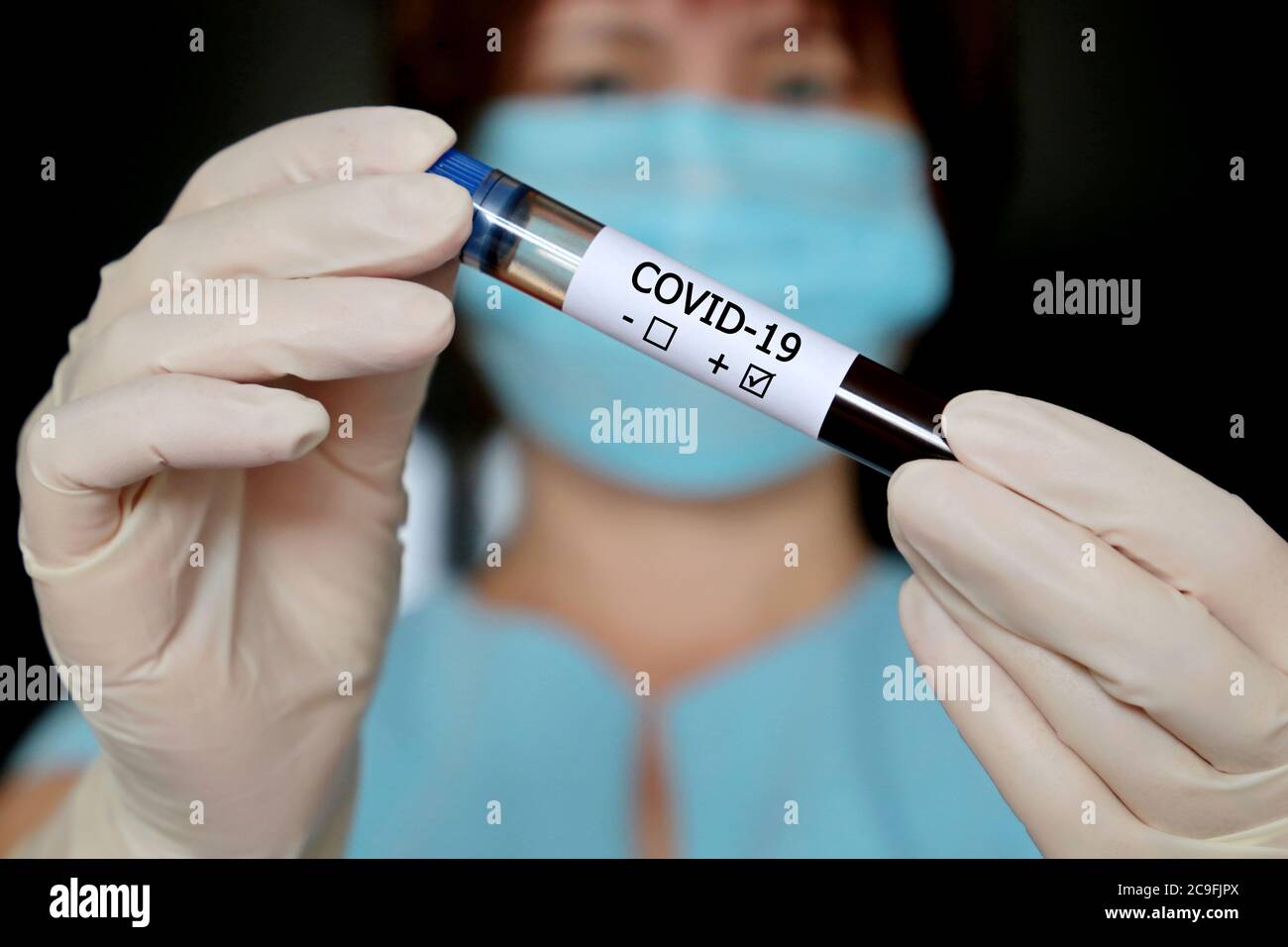 Test tube with covid-19 blood sample in female hands close up, woman in medical mask and gloves holding a vial. Doctor with positive test Stock Photo