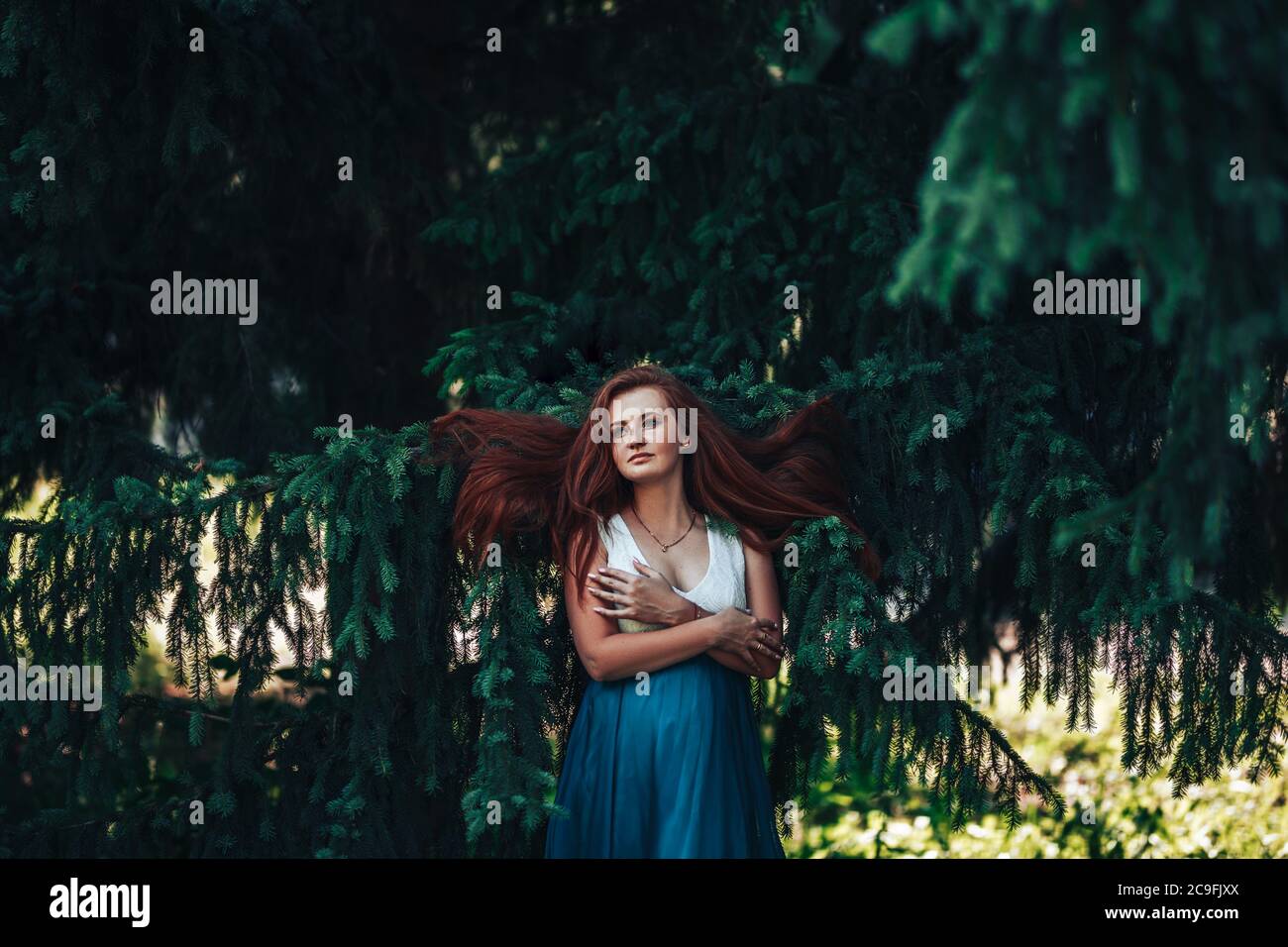 Beautiful red-haired girl on the background of a Christmas tree in a blue dress, spring time, natural beauty Stock Photo