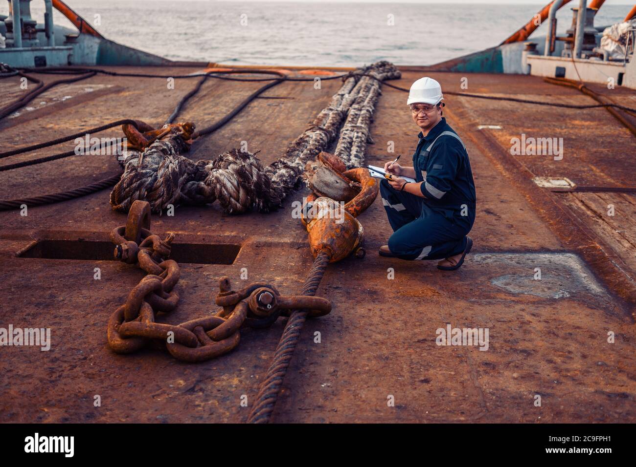 Marine chief officer or chief mate on deck of ship or vessel. He fills up ahts vessel checklist. Ship routine paperwork. He holds VHF walkie-talkie Stock Photo