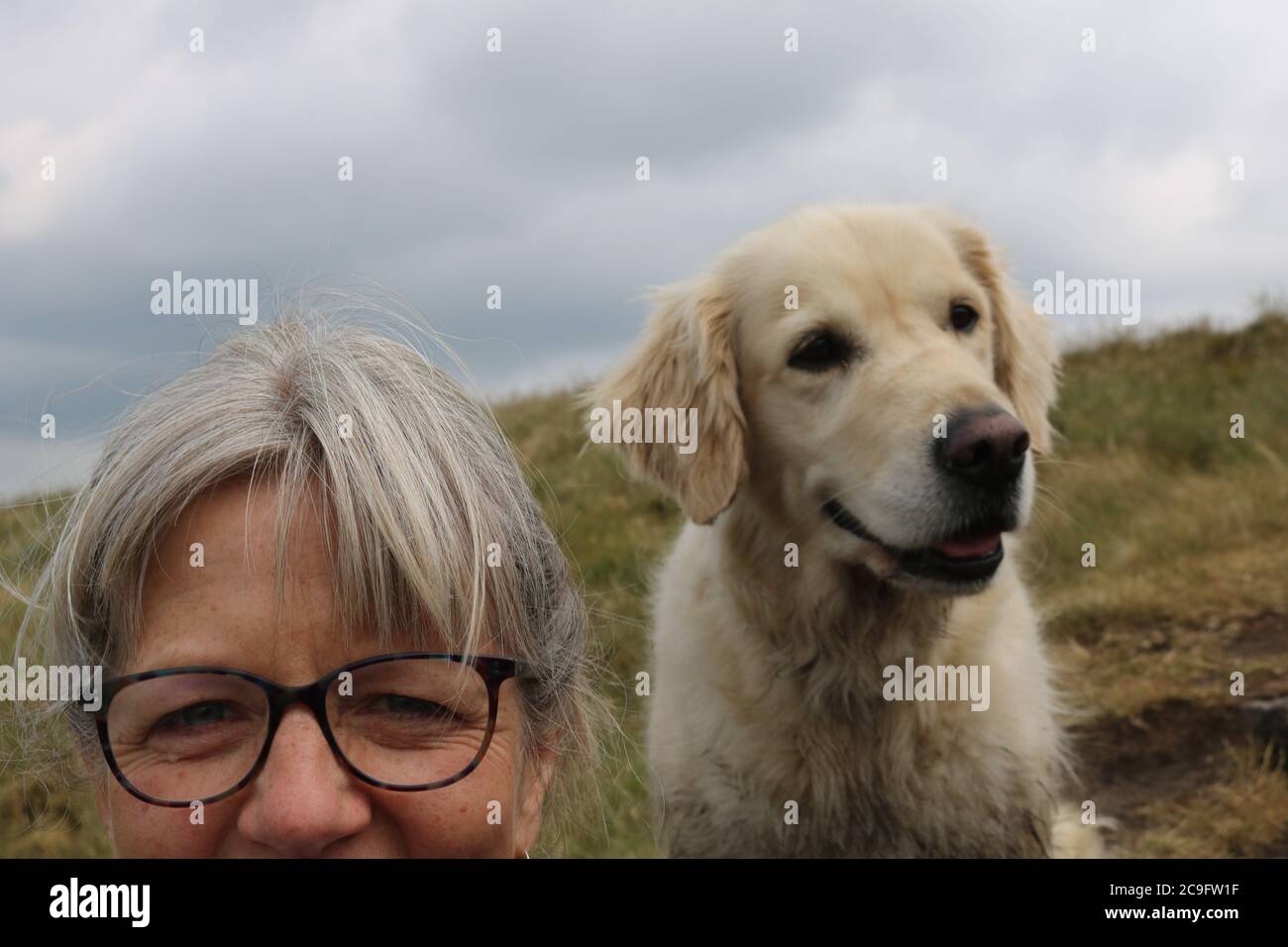 Selfie of Blonde Golden retriever and middle aged blonde lady wearing glasses in close up looking at camera sitting on moorland Stock Photo