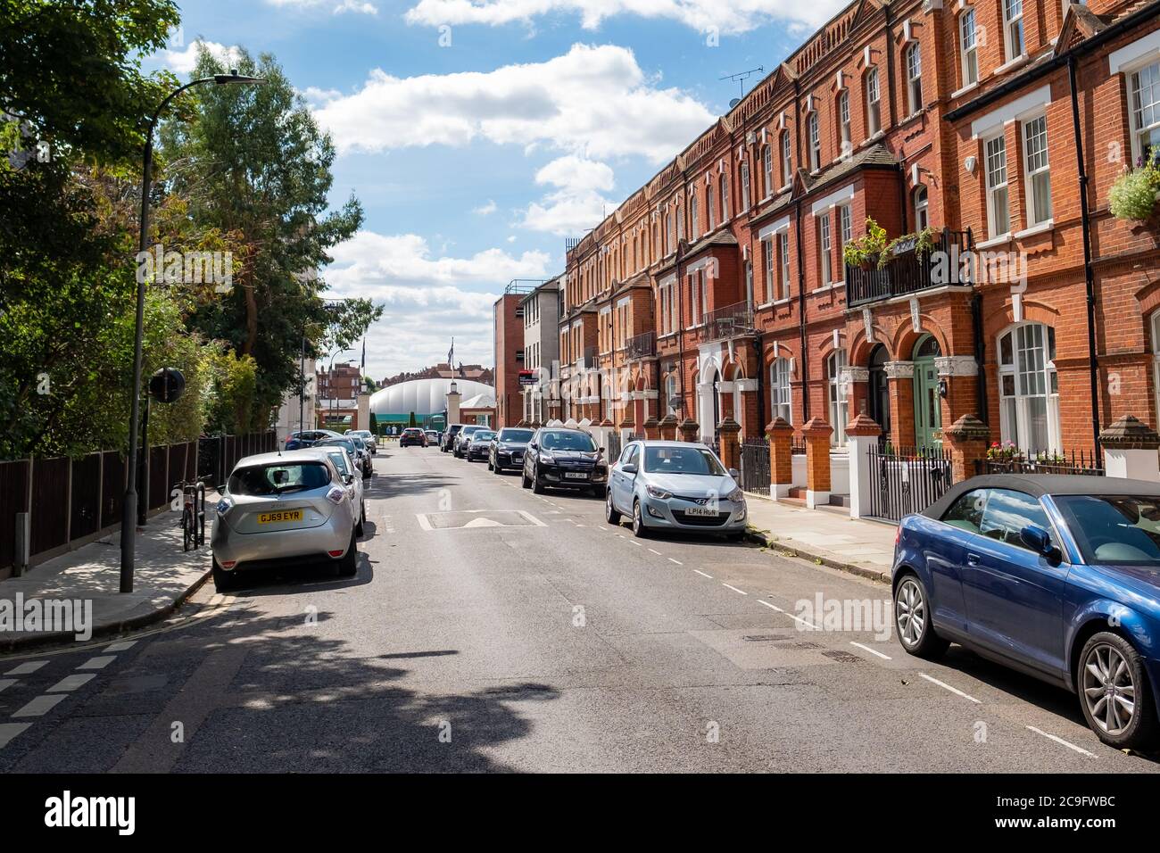 Street of attractive houses by Barons Court Underground Station and the Queens Club tennis venue at the end of the street Stock Photo