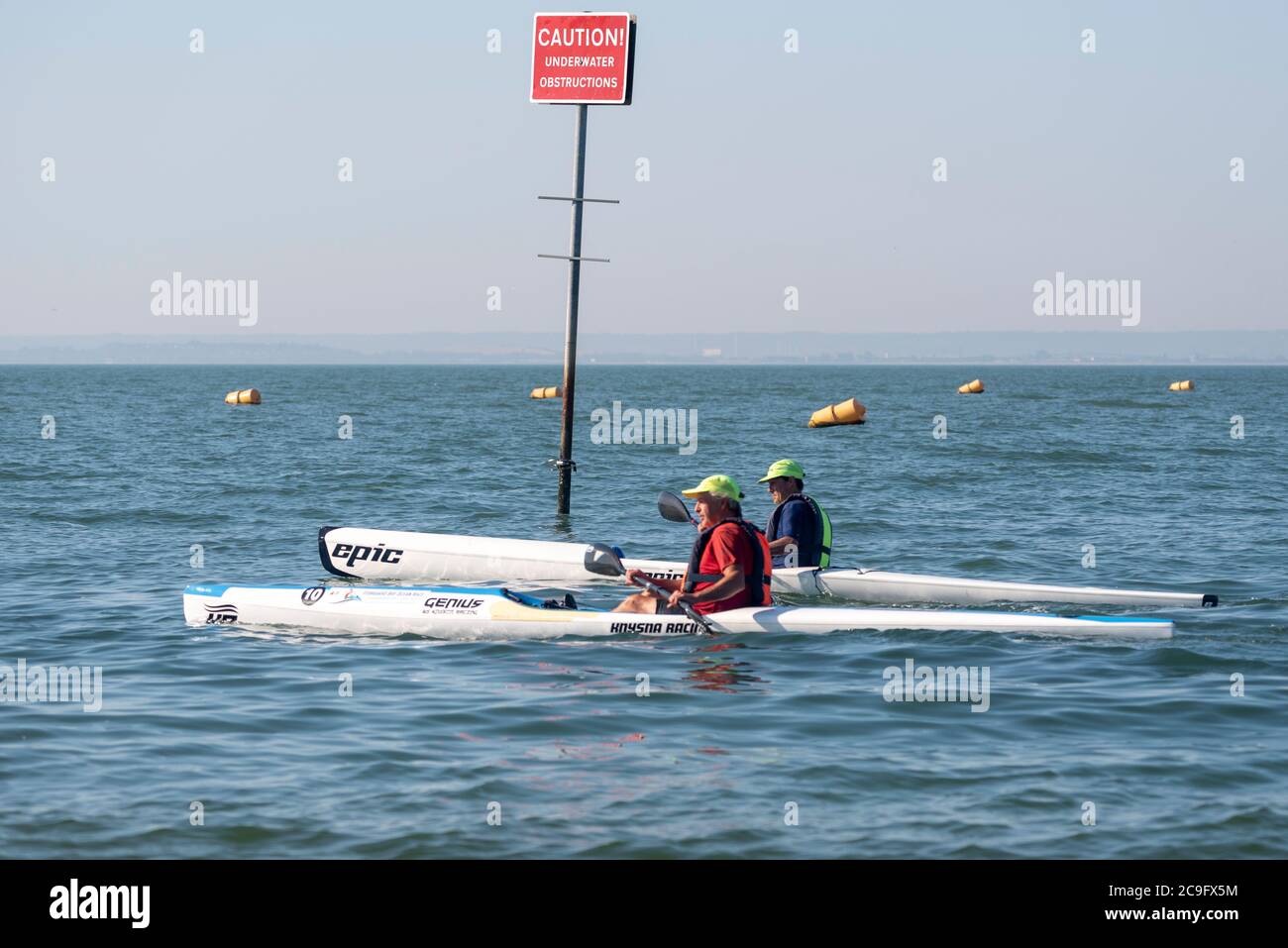 Two white Caucasian males rowing canoes in the Thames Estuary off Thorpe Bay, Southend on Sea, Essex, UK. Canoeing in River. Underwater obstructions Stock Photo