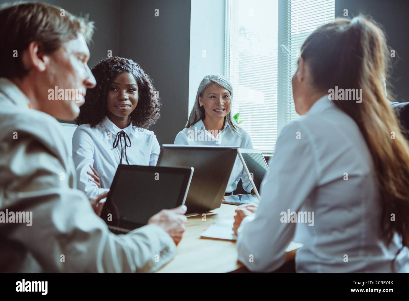 Funny business meeting of diverse team. Happy Multiethnic group of people have conversation sitting at office desk and using computers. Tinted image Stock Photo