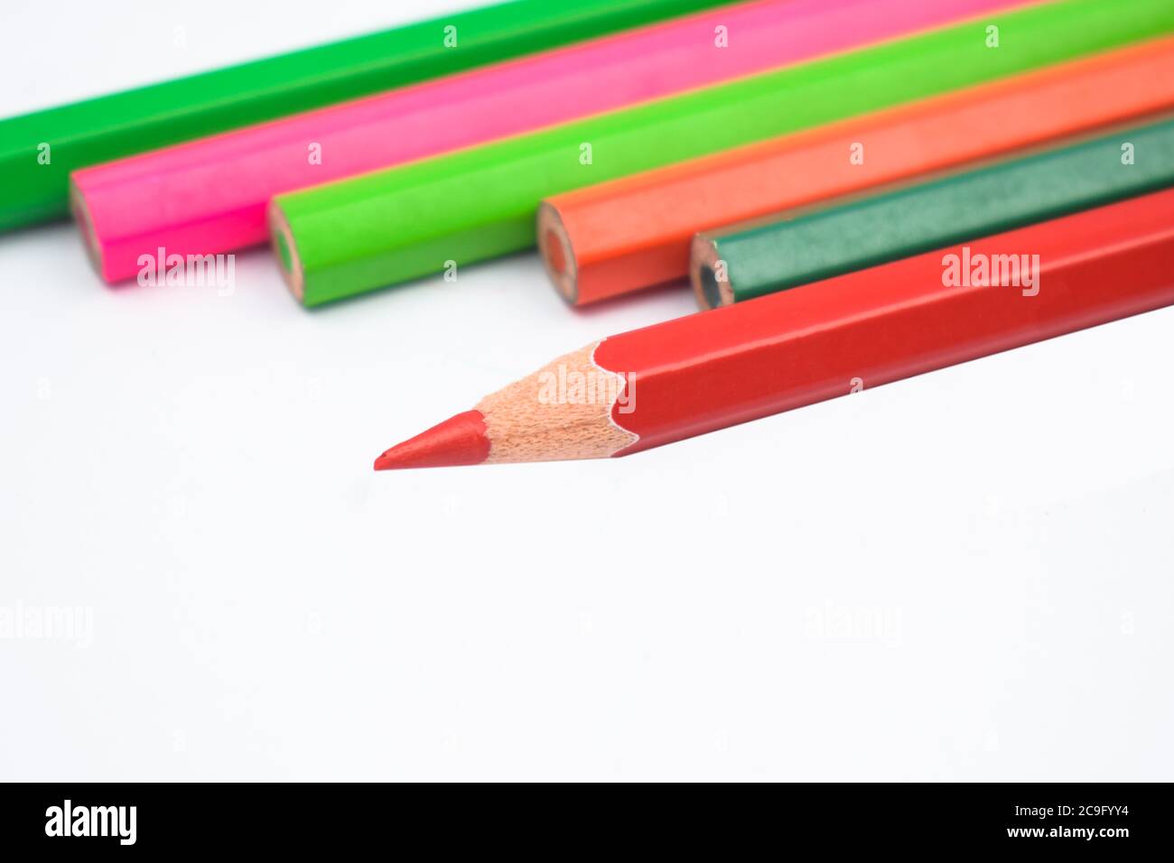 Six different colored wood pencil crayons placed on top of a white paper background Stock Photo