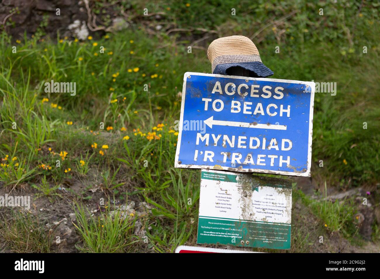 Bilingual sign in Welsh and English pointing to the entrance to a beach in Wales, with sun hat placed on top. Stock Photo