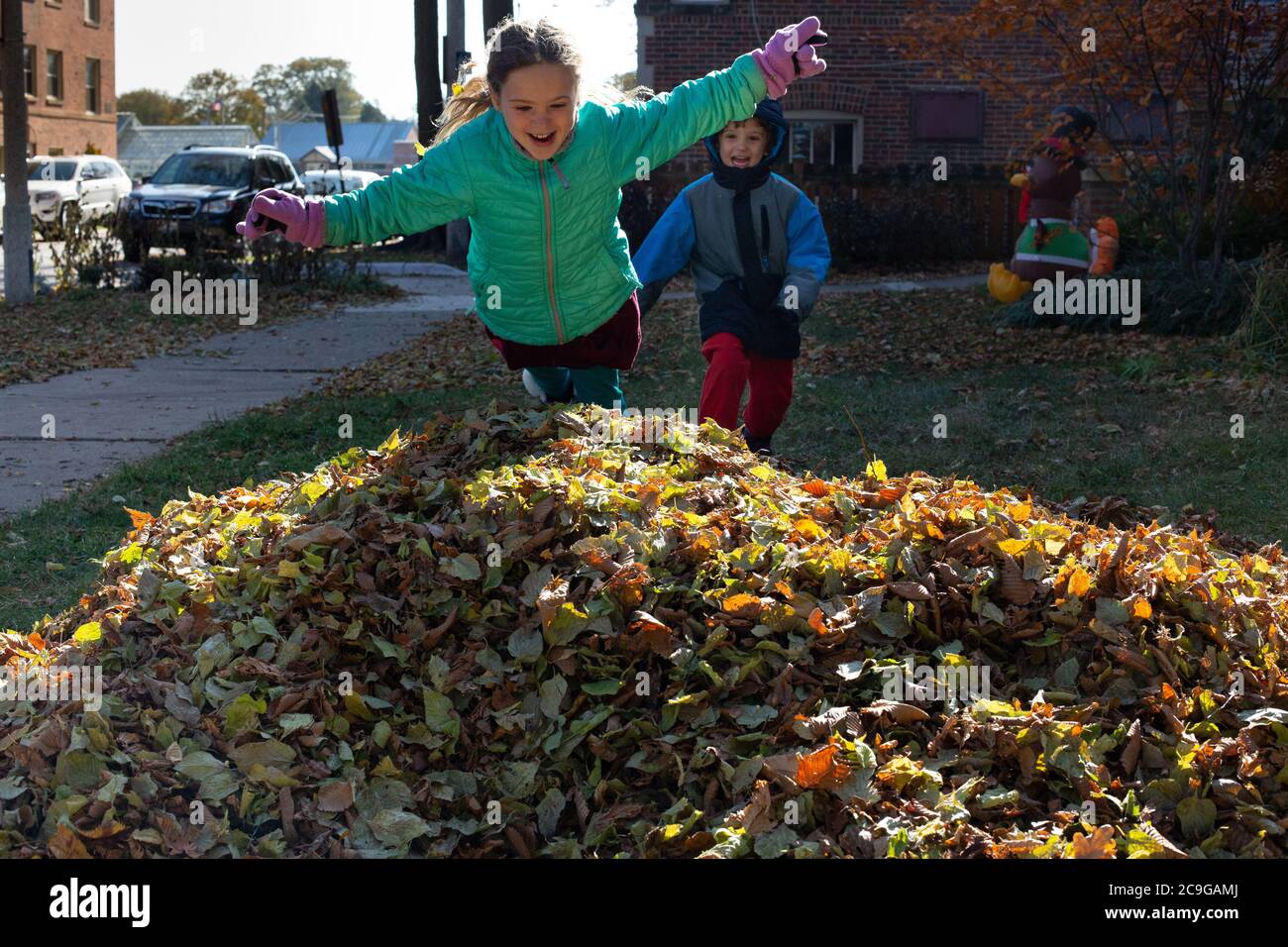 Happy kids jumping into a pile of leaves on a cold fall day Stock Photo