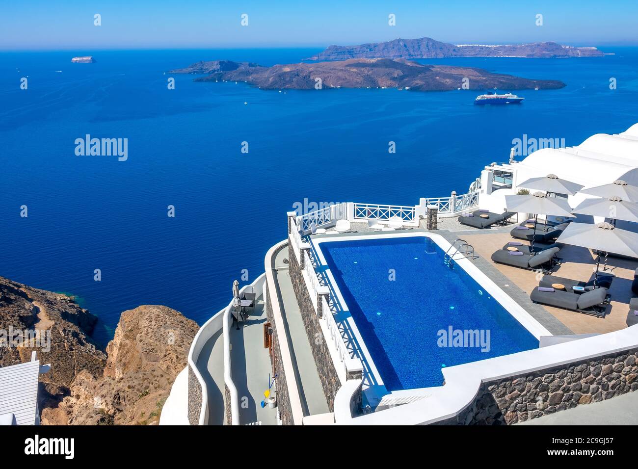 Greece. Thira island. Santorini. Hotel on the high bank in Oia. Pool and sun loungers for relaxation in sunny weather. Seascape Stock Photo
