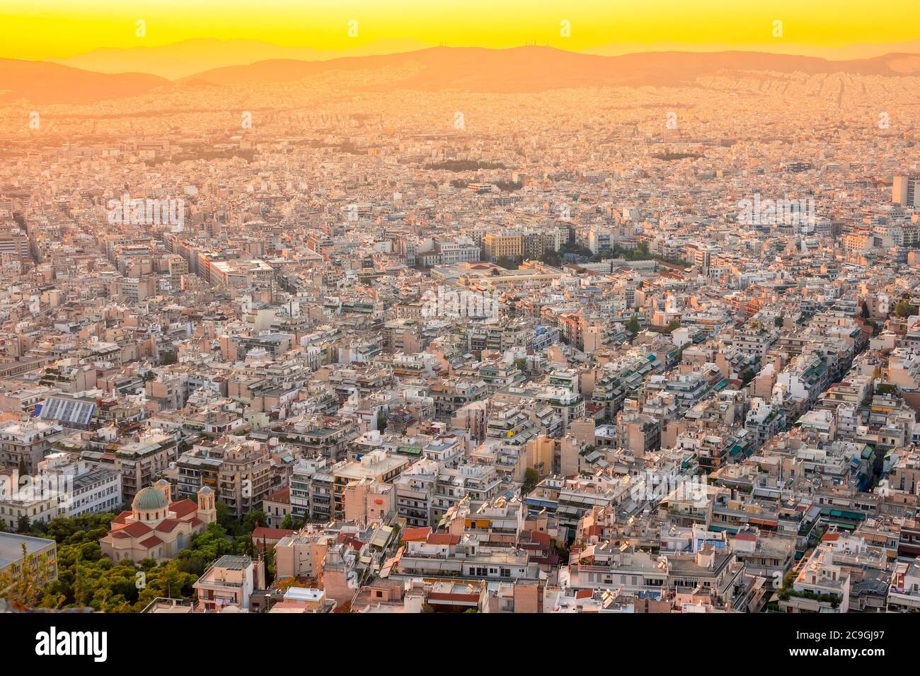 Greece. Warm summer evening over the rooftops of Athens. Residential buildings and narrow streets. Domes of the cathedral with green parks. Aerial vie Stock Photo