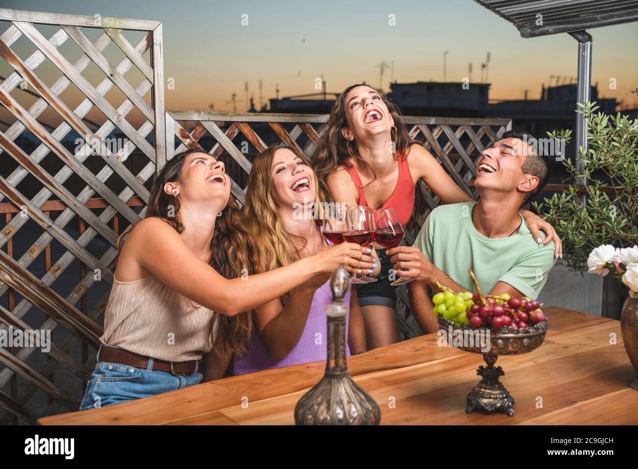 Happy Friends Laughing Loud and Toasting Red Wine Together with White and Red black Grapes on the Table. Balcony Concept with Friends that Spending th Stock Photo