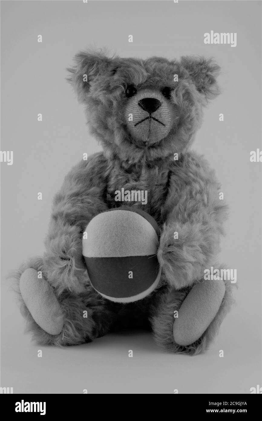 black and white photo of a mohair teddy bear holding a ball Stock Photo