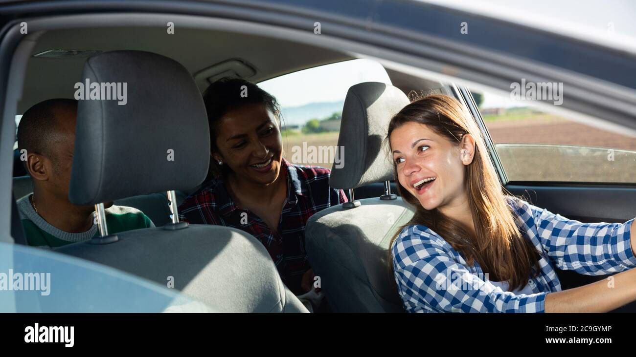 Young adult woman driver talking in car with two friends enjoying road ...