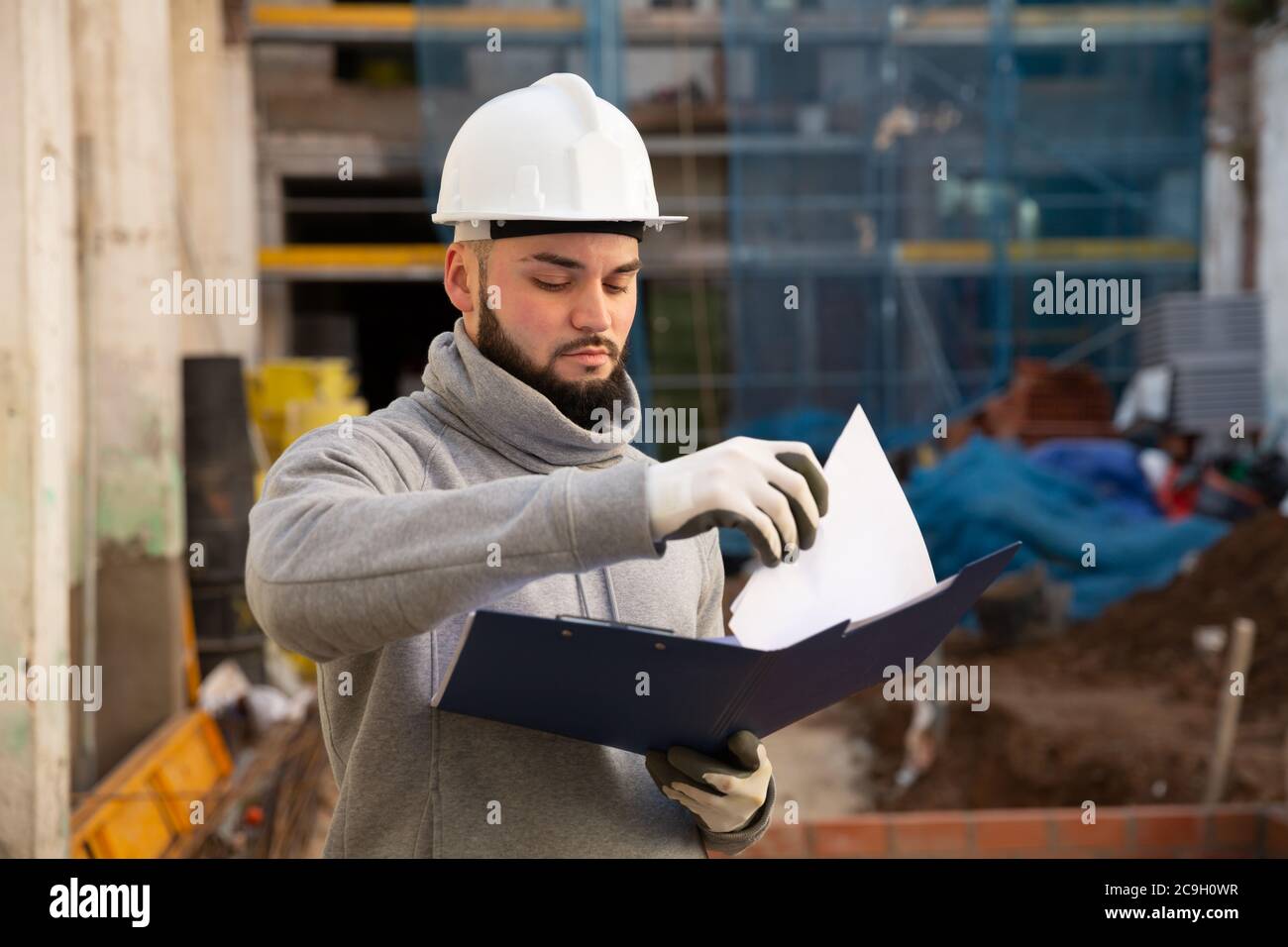 Young bearded foreman making task list during works in building under construction Stock Photo