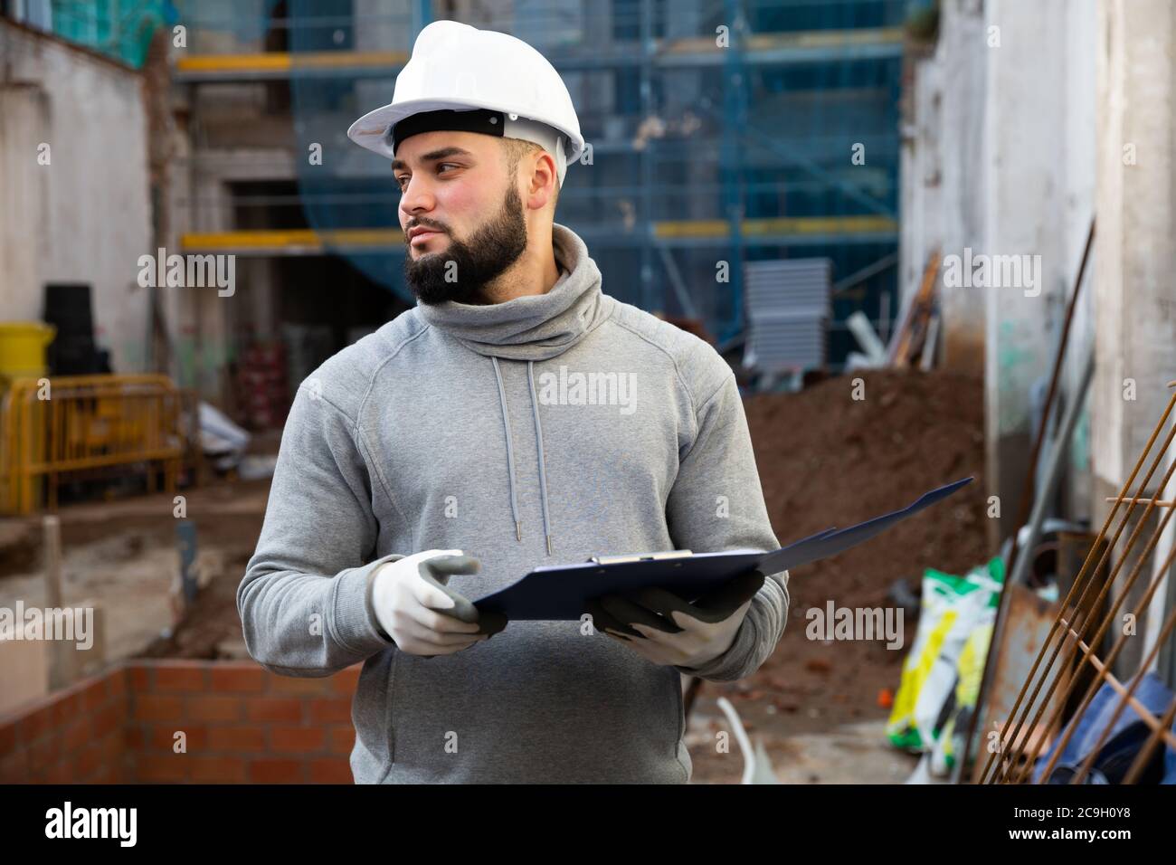 Young bearded foreman making task list during works in building under construction Stock Photo