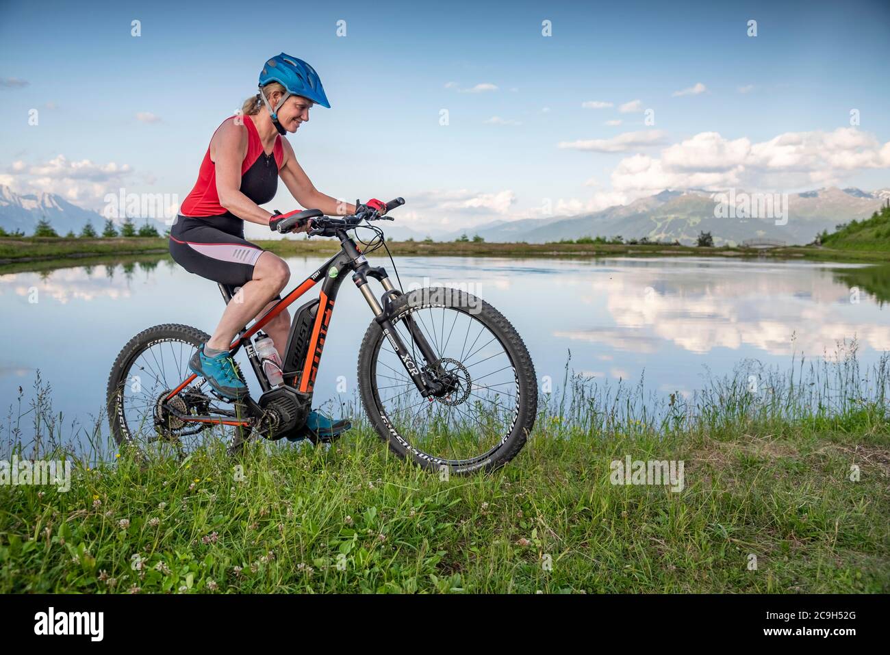 Mountain biker, in her late forties, rides an e-bike along the lake shore against a mountain backdrop, Mutterer Alm, Stubaier Alpen, Mutters, Tyrol Stock Photo