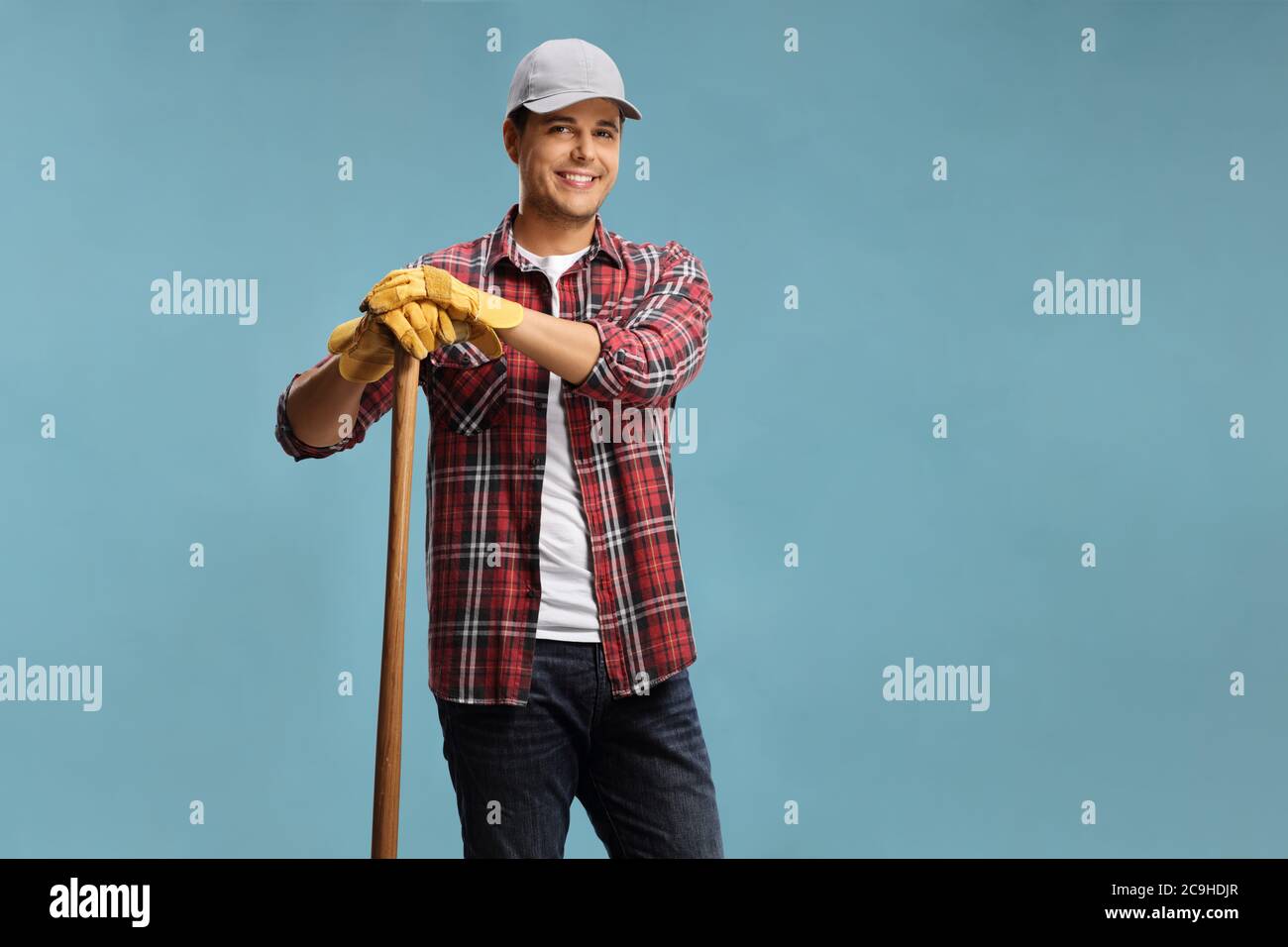 Young male farmer leaning on a wooden stick isolated on a blue background Stock Photo