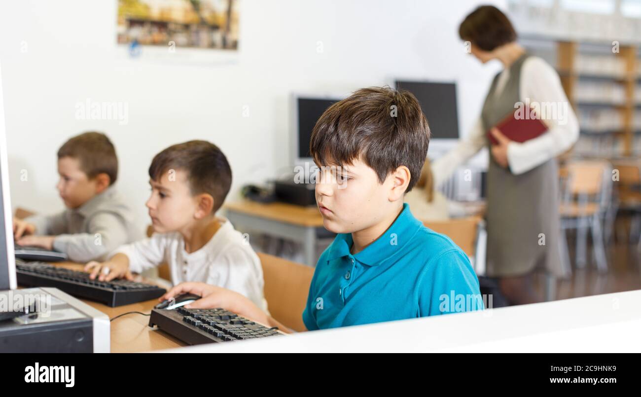 Focused boy studying in computer class of school library on background ...
