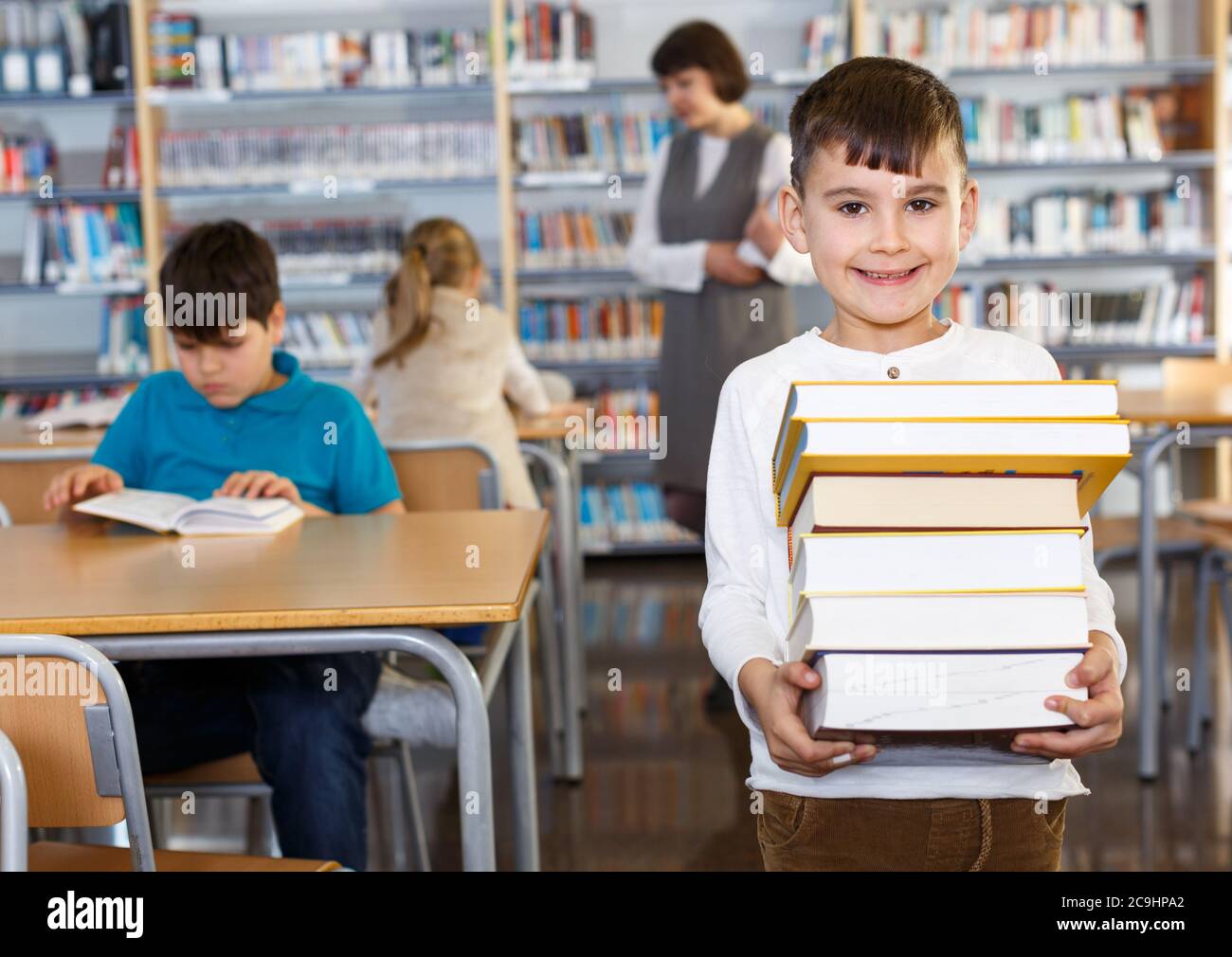 Portrait of smiling preteen boy standing with pile of books in school ...